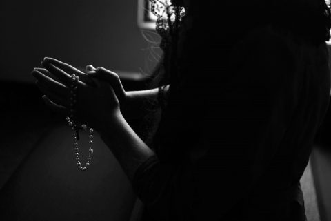 A girl praying in the dark with her rosary.| Photo by Isabella Fischer on Unsplash